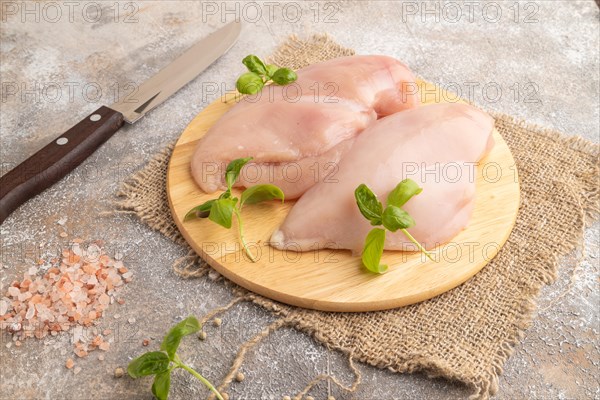 Raw chicken breast with herbs and spices on a wooden cutting board on a brown concrete background.
