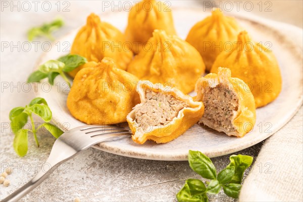 Fried manti dumplings with pepper, basil on gray concrete background and linen textile. Side view,