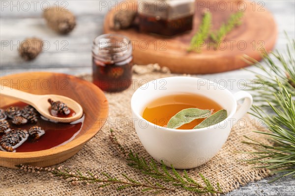 Pine cone jam with herbal tea on gray wooden background and linen textile. Side view, close up,