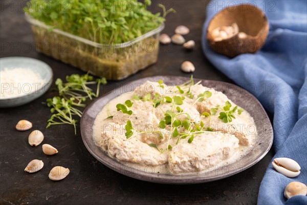Stewed chicken fillets with coconut milk sauce and rucola microgreen on black concrete background