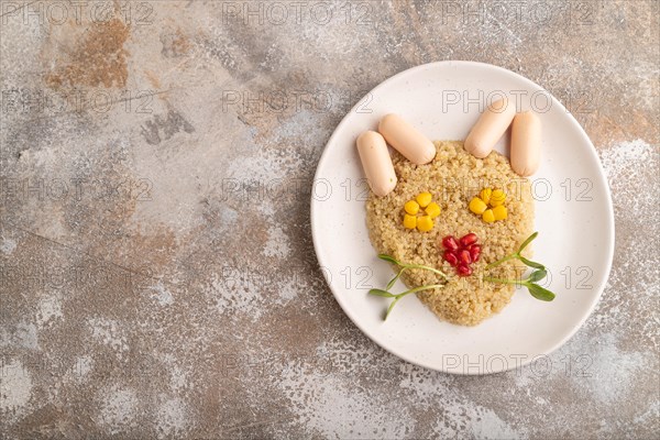 Funny mixed quinoa porridge, sweet corn, pomegranate seeds and small sausages in form of cat face