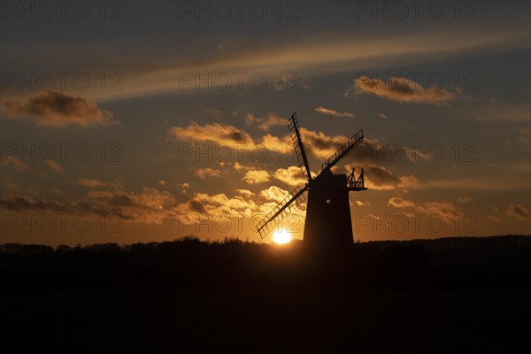 Windmill silhouetted at sunset with a red sky and clouds, Burnham Ovary Staithe, Norfolk, England,