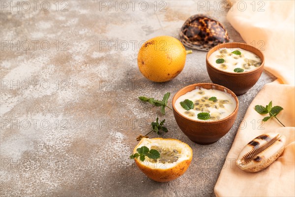 Yoghurt with granadilla and mint in clay bowl on brown concrete background and orange linen textile