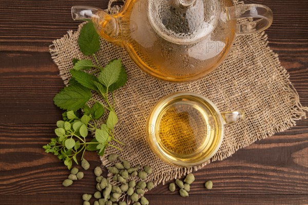 Green oolong tea with herbs in glass on brown wooden background and linen textile. Healthy drink