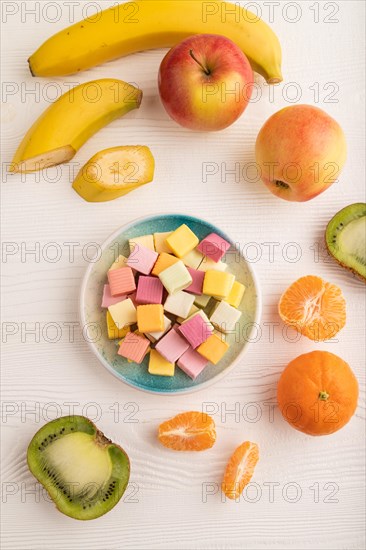 Various fruit jelly chewing candies on plate on white wooden background. apple, banana, tangerine,