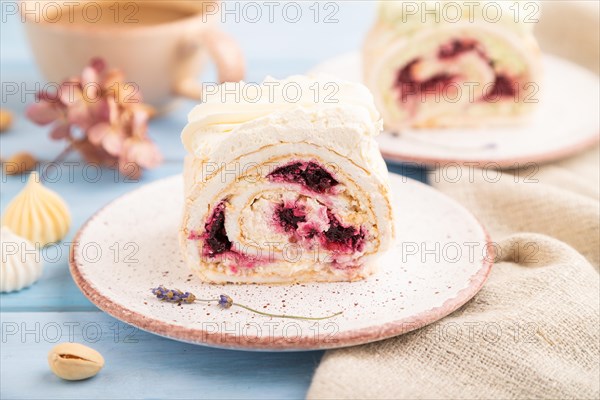 Roll biscuit cake with cream cheese and jam, cup of coffee on blue wooden background and linen