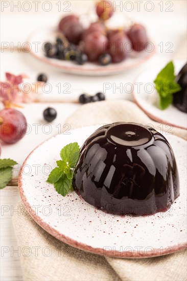 Black currant and grapes jelly on white wooden background and linen textile. side view, close up,