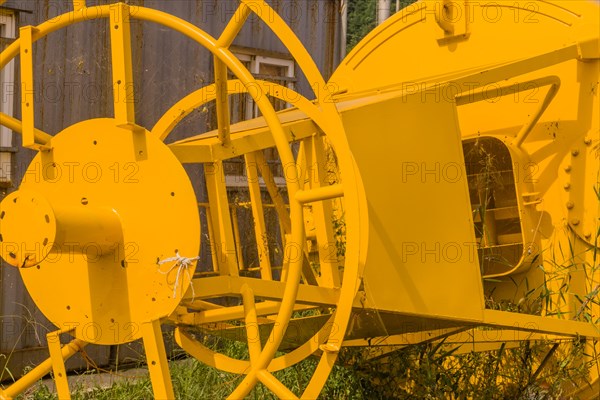 Bottom steel framework of ocean buoy laying in grass next to old rusty storage building in fishing
