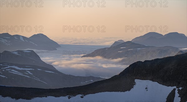 Mountain panorama with clouds in the valley, mountain peaks in soft light at sunset, view from the
