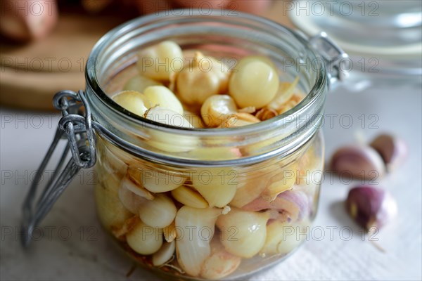 An open preserving jar full of pickled shallots and garlic cloves on a table, AI generated, AI