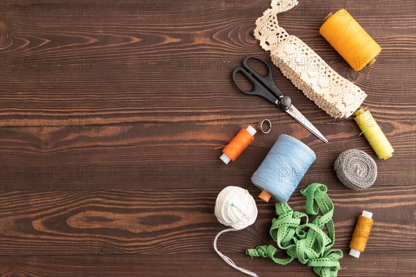 Sewing accessories: scissors, thread, thimbles, braid on brown wooden background. Top view, flat
