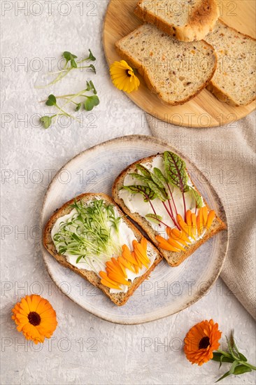 White bread sandwiches with cream cheese, calendula petals and microgreen on gray concrete