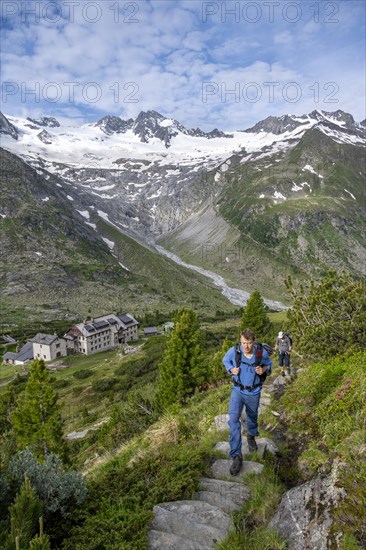 Two mountaineers on a hiking trail in a picturesque mountain landscape with alpine roses, in the