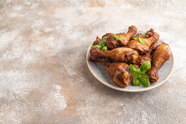 Smoked chicken legs with herbs and spices on a ceramic plate on a brown concrete background. Side