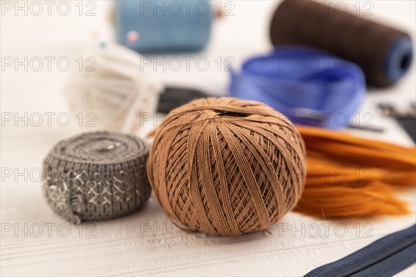 Sewing accessories: scissors, thread, thimbles, braid on white wooden background. Side view, close