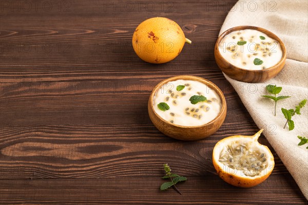 Yoghurt with granadilla and mint in wooden bowl on brown wooden background and linen textile. side