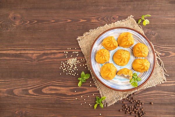 Fried manti dumplings with pepper, basil on brown wooden background and linen textile. Top view,