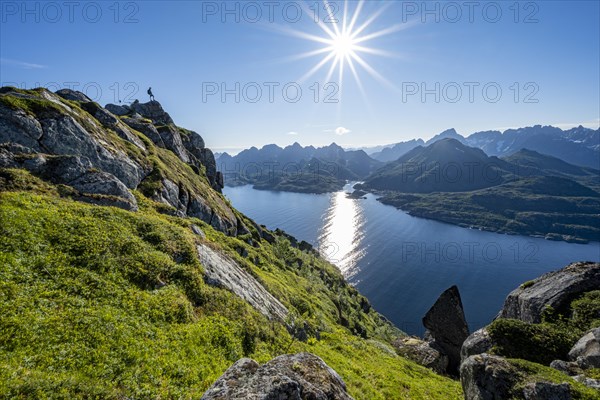 Mountaineer on the summit of Dronningsvarden or Stortinden, behind sea and fjord Umvagsundet,
