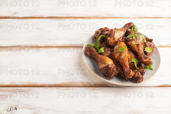 Smoked chicken legs with herbs and spices on a ceramic plate on a white wooden background. Side