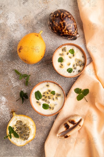 Yoghurt with granadilla and mint in clay bowl on brown concrete background and orange linen textile