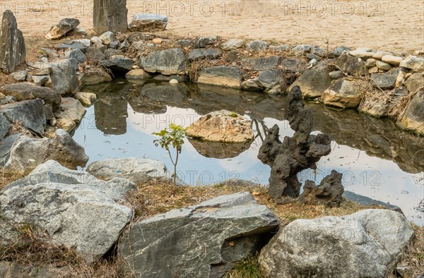Piece of basalt shaped like tree next to small man made pond surrounded by granite boulders in