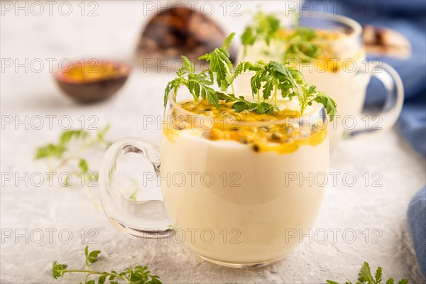 Yogurt with passionfruit and marigold microgreen in glass on gray concrete background with blue
