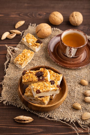 Traditional candy nougat with nuts and sesame with cup of green tea on brown wooden background and