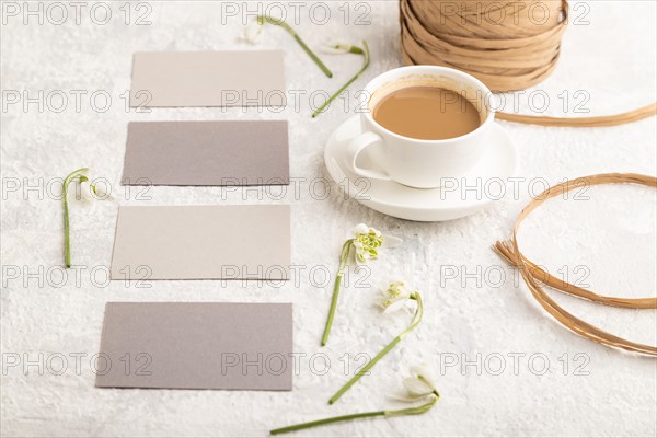 Gray paper business card mockup with spring snowdrop galanthus flowers and cup of coffee on gray
