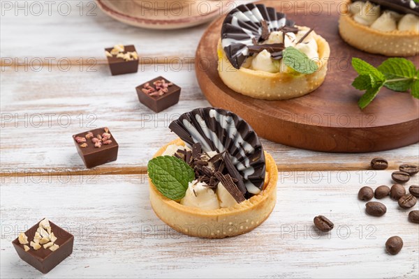 Sweet tartlets with chocolate and cheese cream with cup of coffee on a white wooden background and