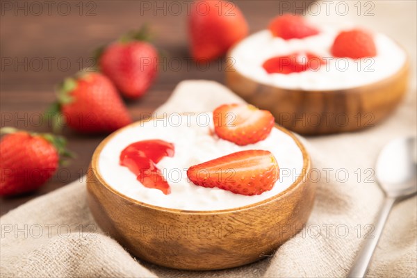 Grained cottage cheese with strawberry jam on brown wooden background and linen textile. side view,