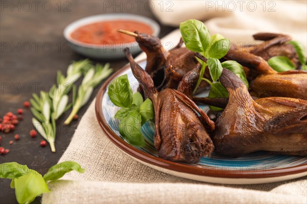 Smoked quails with herbs and spices on a ceramic plate with linen textile on a black concrete