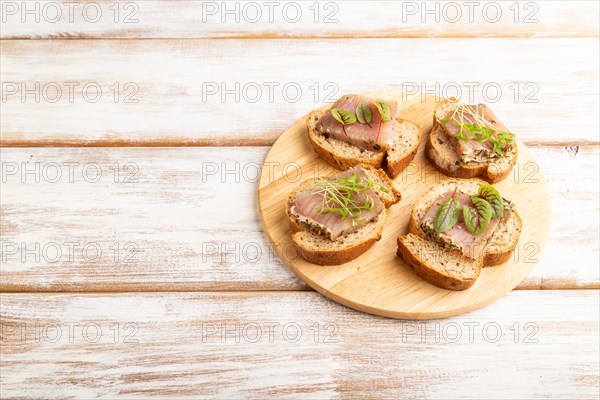 Bread sandwiches with jerky salted meat, sorrel and cilantro microgreen on white wooden background.