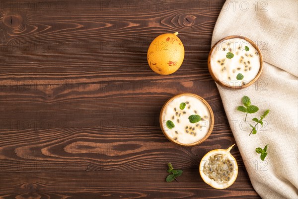 Yoghurt with granadilla and mint in wooden bowl on brown wooden background and linen textile. top