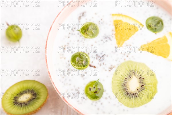 Yogurt with kiwi, gooseberry, chia in ceramic bowl on gray concrete background and orange linen