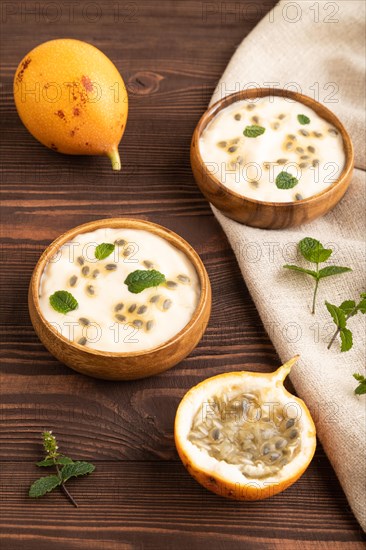 Yoghurt with granadilla and mint in wooden bowl on brown wooden background and linen textile. side
