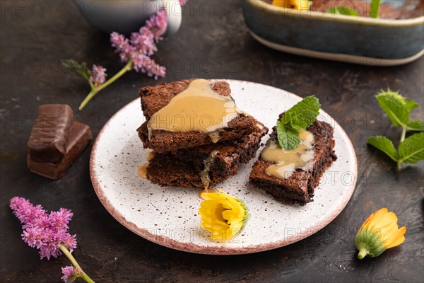 Chocolate brownie with caramel sauce with a cup of coffee on black concrete background. side view,