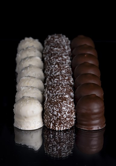 Row of chocolate kisses covered with dark and light chocolate, grated coconut, reflection, dark