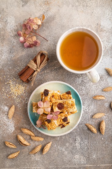 Traditional candy nougat with nuts and sesame with cup of green tea on brown concrete background.