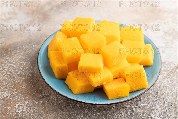Dried and candied mango cubes on blue plate on brown concrete background. Side view, close up,