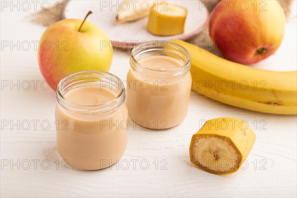 Baby puree with fruits mix, apple, banana infant formula in glass jar on white wooden background.
