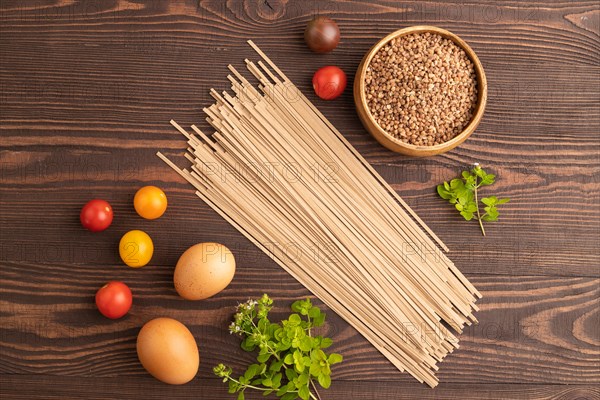 Japanese buckwheat soba noodles with tomato, eggs, spices, herbs on brown wooden background. Top