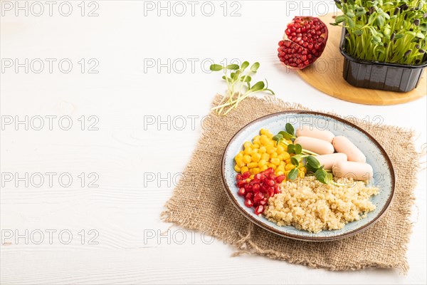 Mixed quinoa porridge, sweet corn, pomegranate seeds and small sausages on white wooden background.