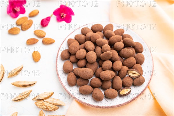 Almond in chocolate dragees on ceramic plate and a cup of coffee on white concrete background and