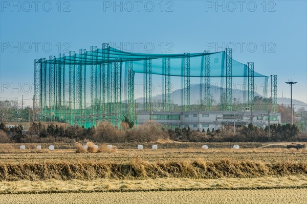 Golf driving range constructed of metal trussed columns and green netting in rural farming