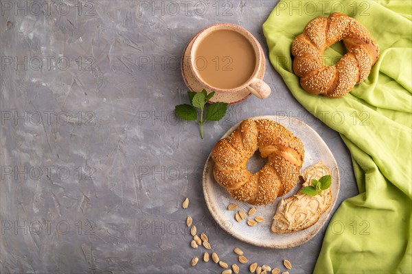 Homemade sweet bun with peanut butter and cup of coffee on a gray concrete background and green