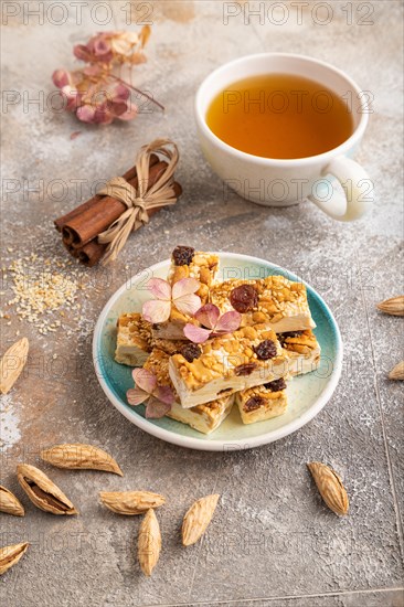 Traditional candy nougat with nuts and sesame with cup of green tea on brown concrete background.