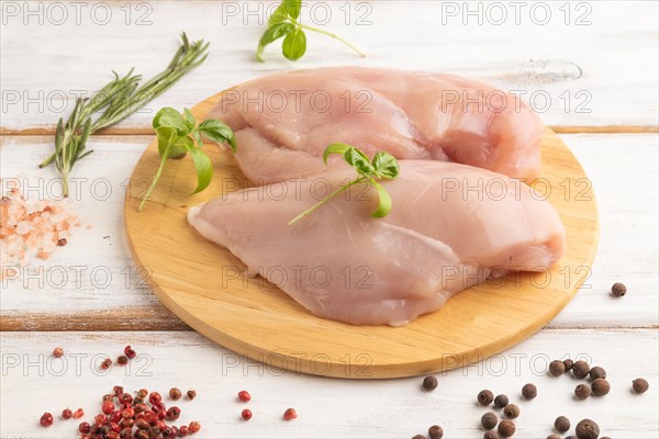 Raw chicken breast with herbs and spices on a wooden cutting board on a white wooden background.