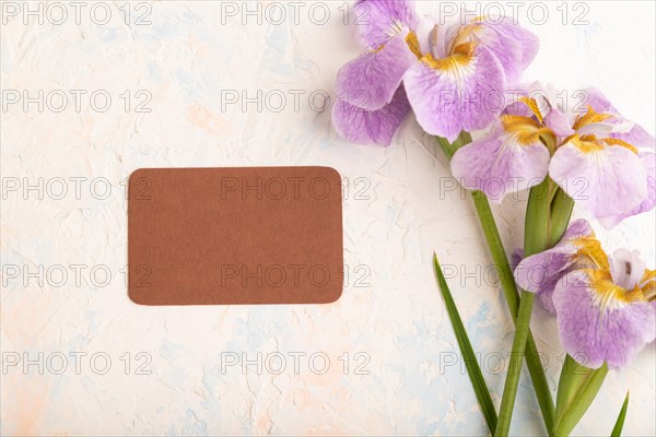 Brown business card with lilac iris flowers on white concrete background. top view, flat lay, copy