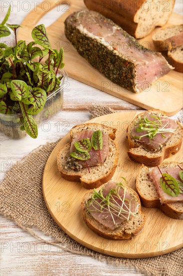 Bread sandwiches with jerky salted meat, sorrel and cilantro microgreen on white wooden background