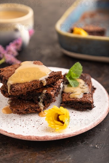 Chocolate brownie with caramel sauce with a cup of coffee on black concrete background. side view,
